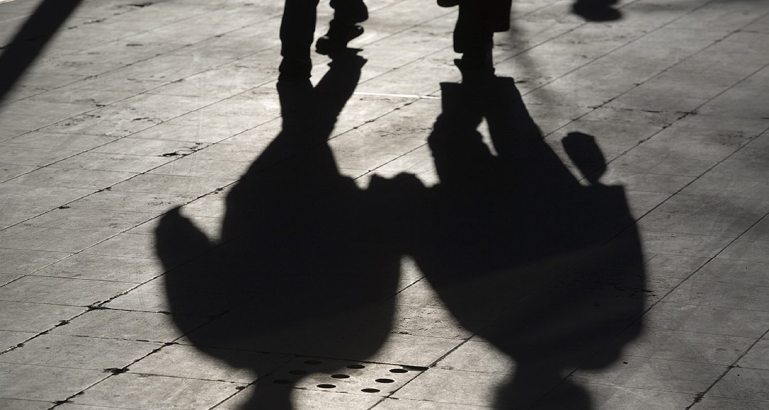 sun casting shadow over two people walking on the street